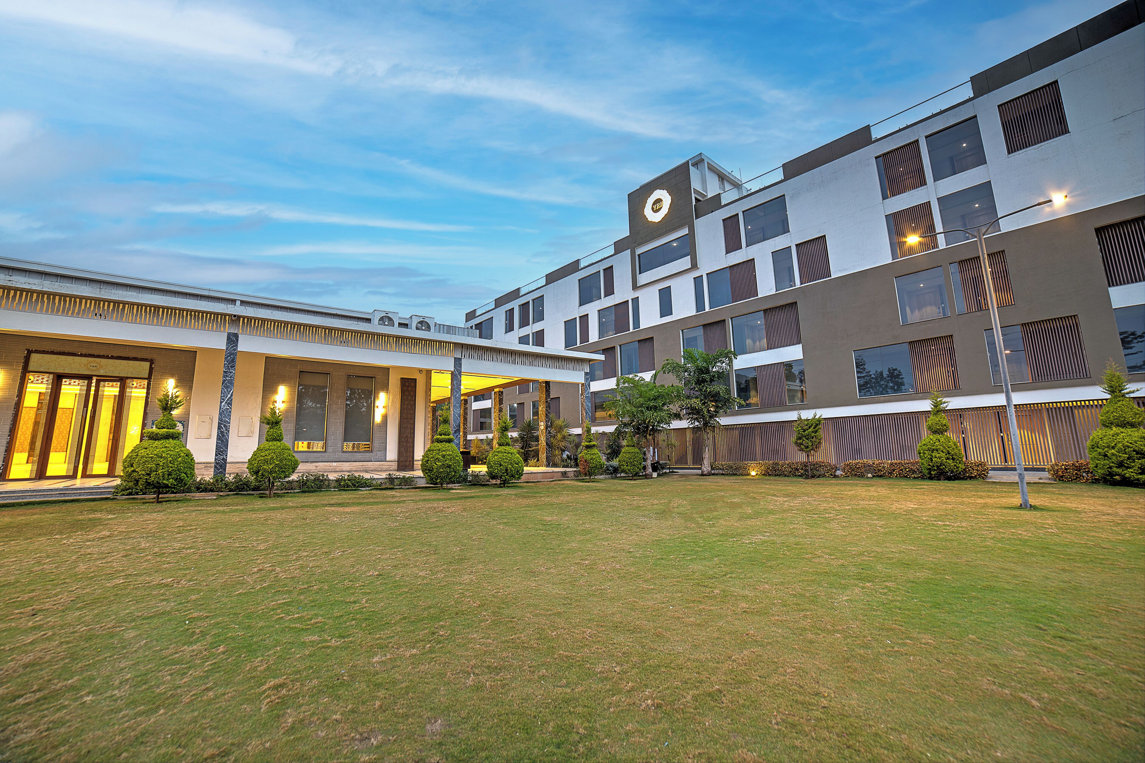 A modern hotel with a spacious courtyard, a well-maintained lawn, and a variety of trees and shrubs.