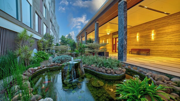 A hotel courtyard with a pond, potted plants, and a wooden bench. - VRR Hotel's And Convention Centre (Anekal)