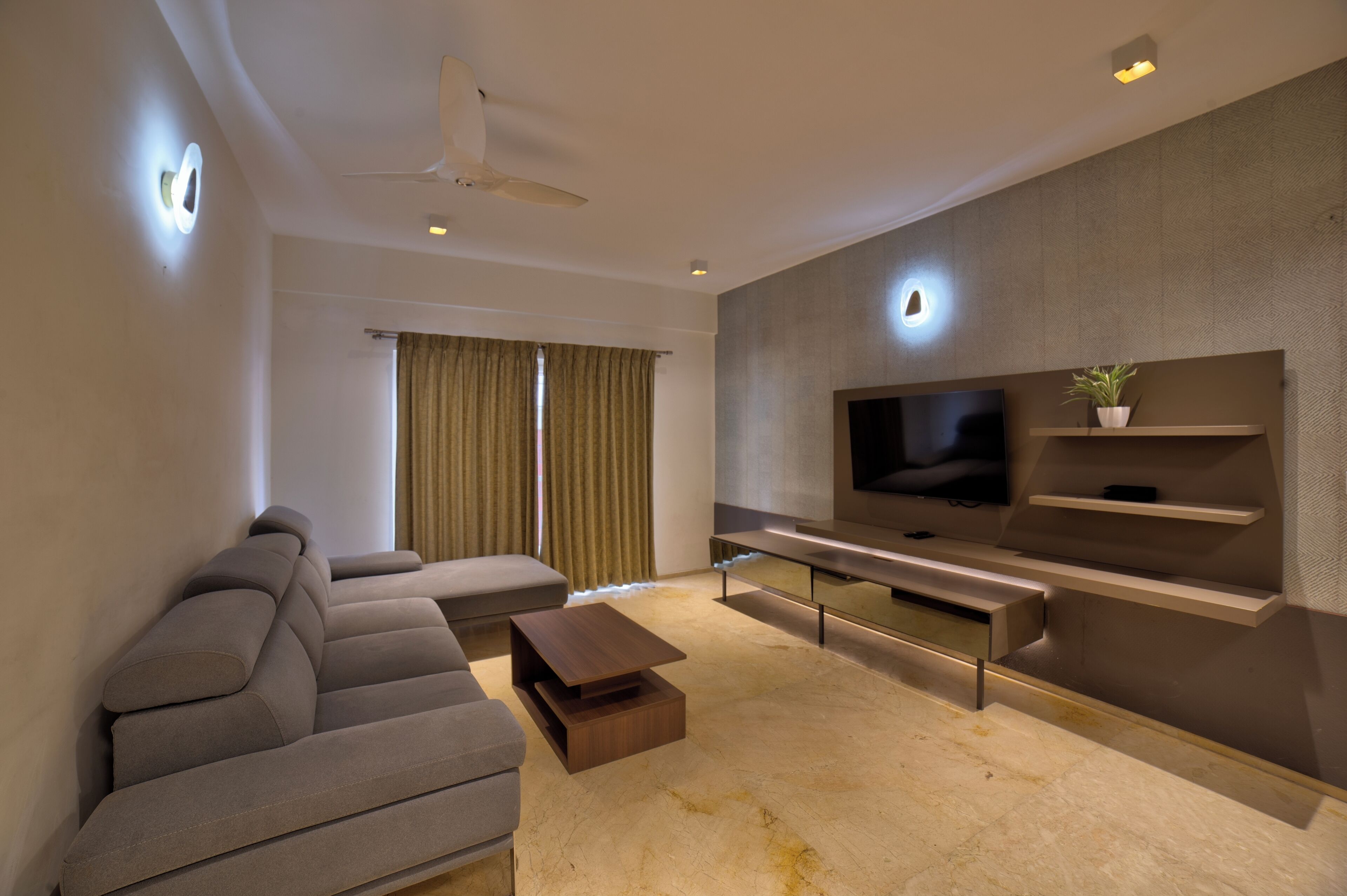 A modern living room with a flat-screen TV, a sofa, a coffee table, and a ceiling fan.