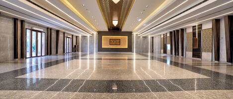 A spacious, modern lobby with a polished marble floor, a central chandelier, and a framed artwork on the wall.