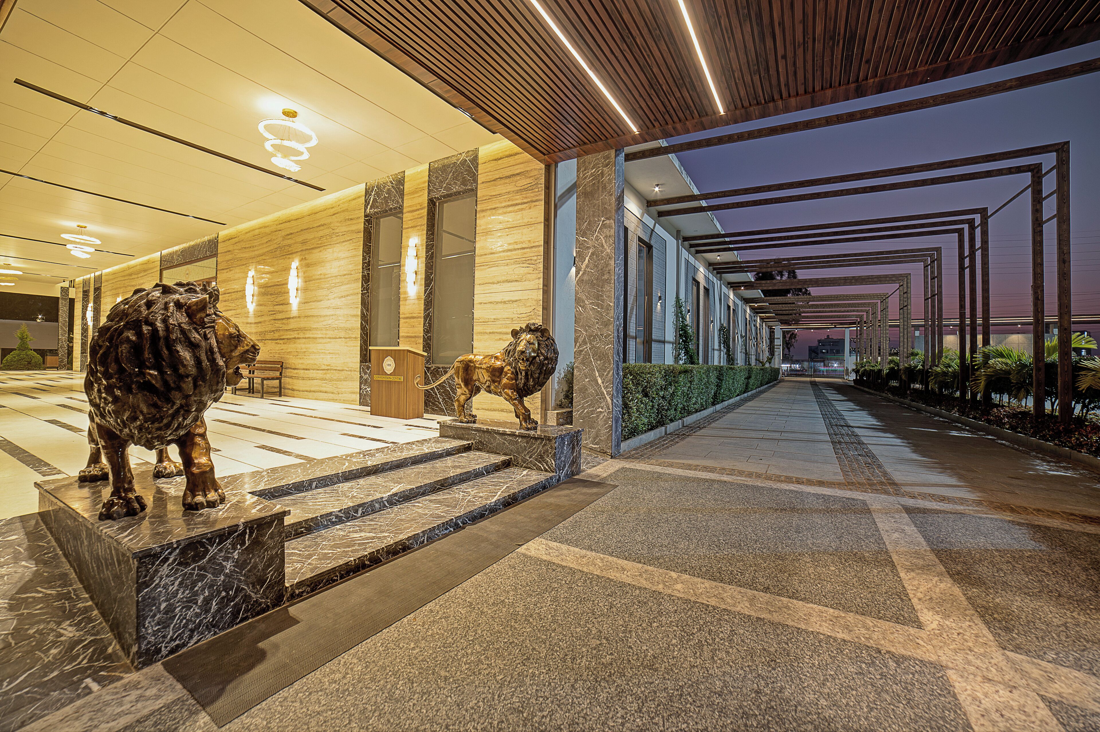 A modern hotel lobby with marble flooring, a lion statue, and a view of the cityscape at dusk.