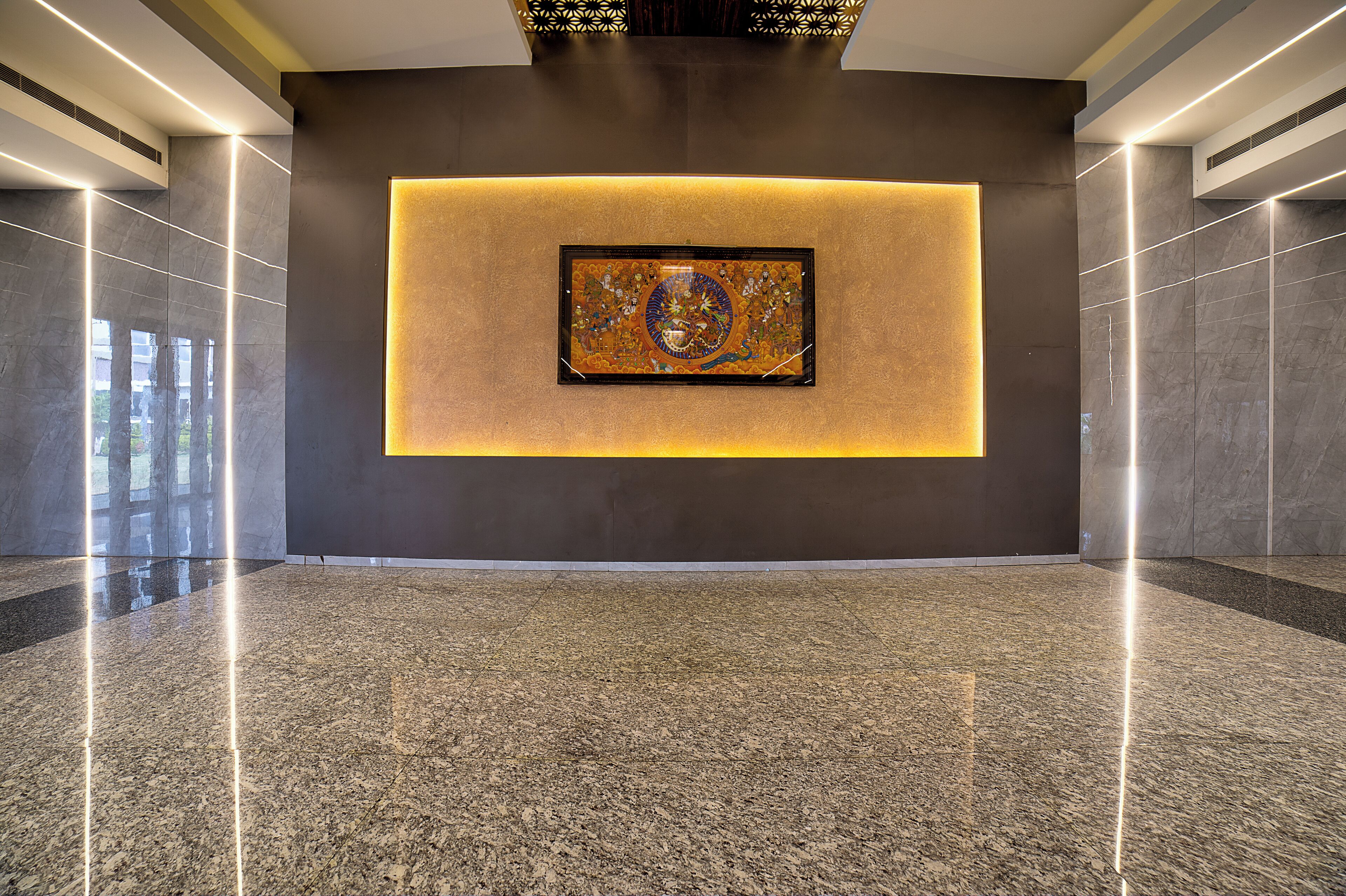 A spacious lobby with a polished granite floor, a large framed artwork on the wall, and modern lighting fixtures.
