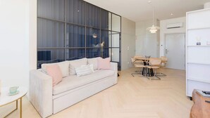 A modern living room with a sofa, a dining table with chairs, and a large window with curtains. - Liiiving in Porto - Modern Coastline Apartment (Porto)