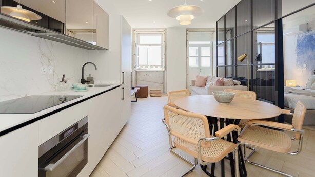 A modern kitchen with a central island, built-in oven, and a dining area with a round table and wicker chairs. - Liiiving in Porto - Modern Coastline Apartment (Porto)