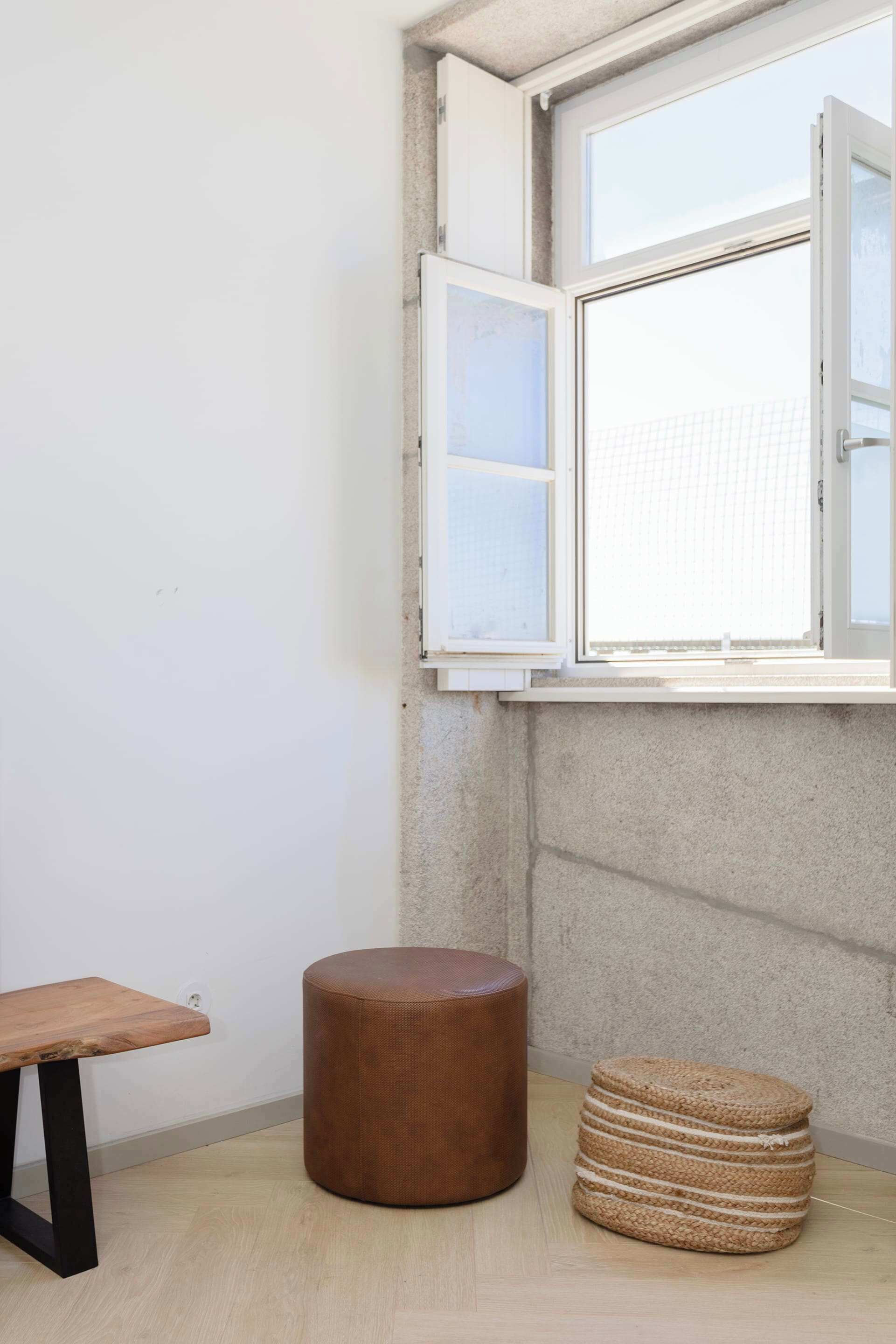 A corner room with a window, a wooden bench, and a round stool.