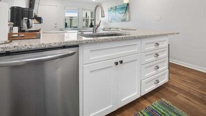 A modern kitchen with white cabinetry, a granite countertop, and a stainless steel dishwasher.