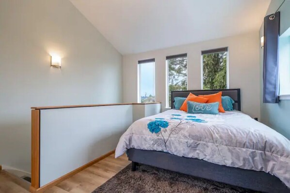 A bedroom with a bed, a nightstand, a wall-mounted light, and a window.