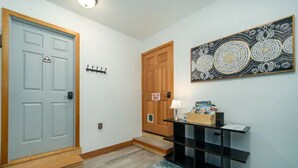 Un couloir avec une porte bleu clair, une porte en bois, une console noire avec une lampe et un tapis à motifs.