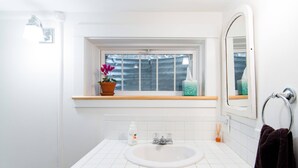 A bathroom with a white sink, a window with a view, a mirror, and a towel rack. - Renovated basement studio in historic Mapleton Hill. (Boulder)