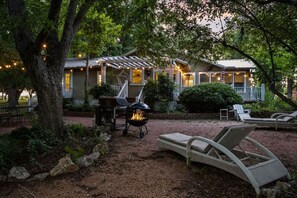 Un patio exterior acogedor con una parrilla, sillones de descanso y una casa con porche cubierto.
