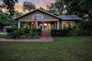 A two-story building with a front porch, a flag, and a brick pathway leading to the entrance. - Nut House Countryside Pecan Farm 14 ac San Marcos (Maxwell)
