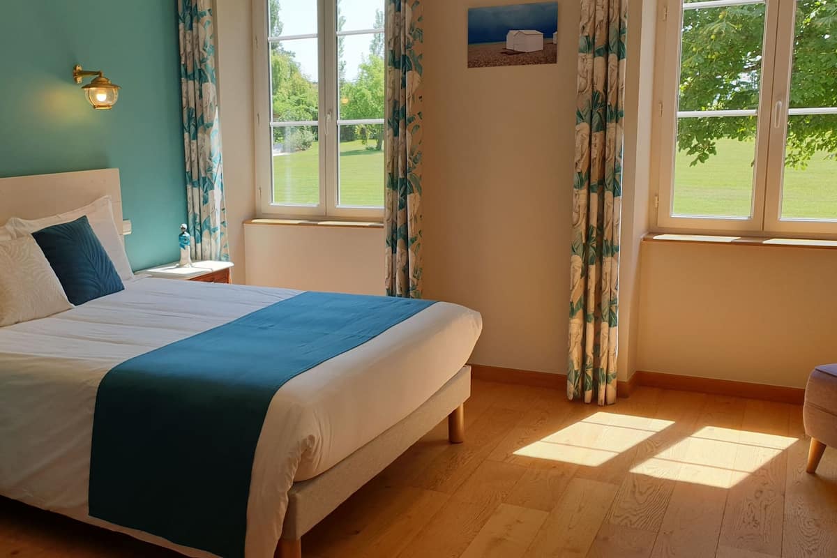 Un dormitorio con cama, dos luces en la pared, una mesita de noche, una ventana con cortinas y vistas al exterior.