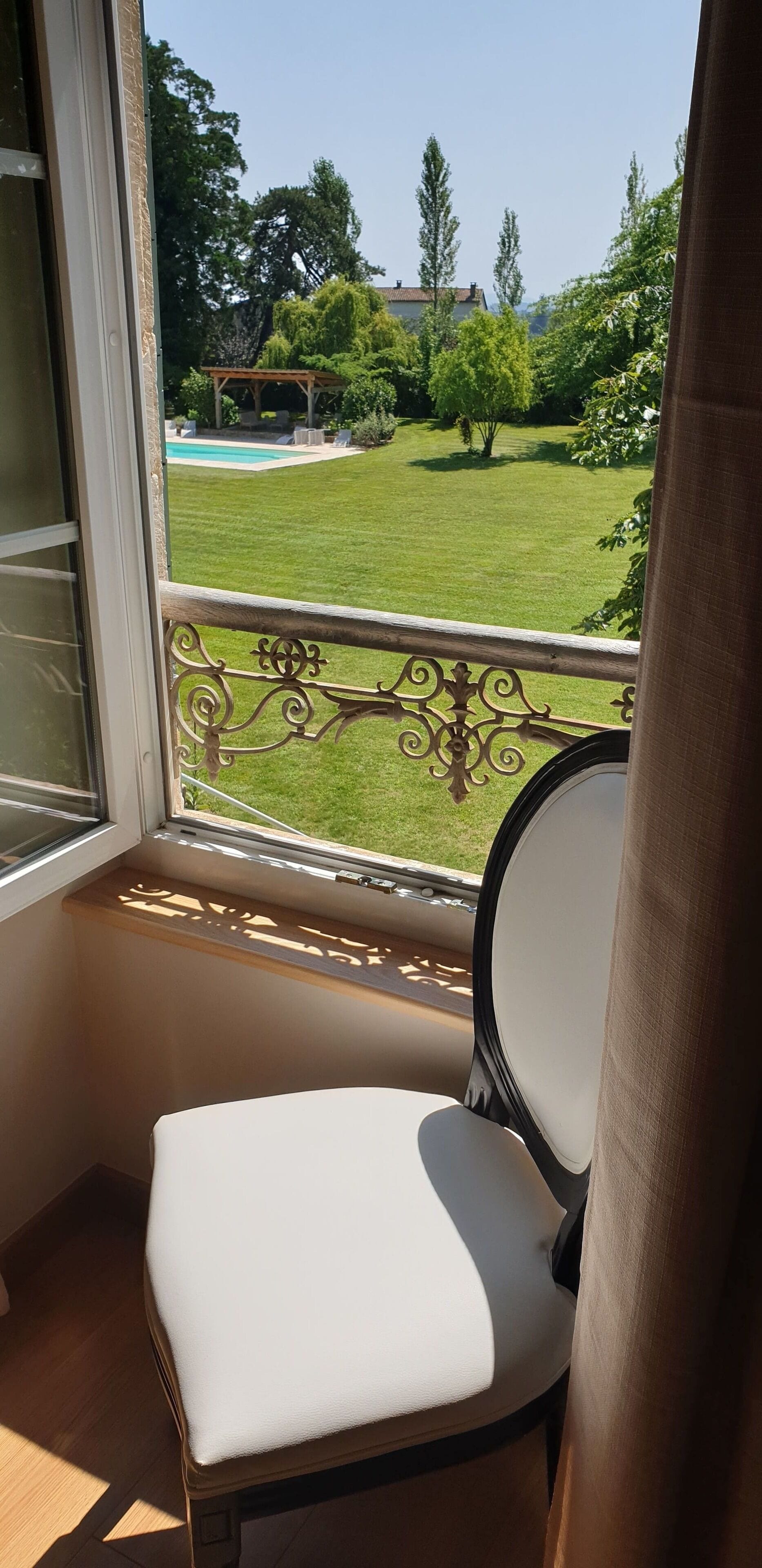 Un balcon offrant une vue sur une pelouse bien entretenue, une piscine et une pergola en bois.