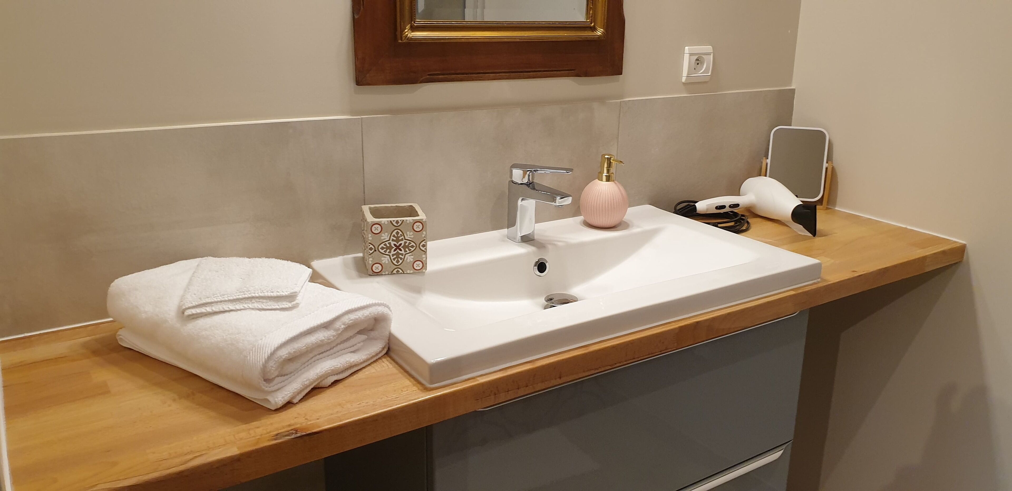 Une salle de bain avec un lavabo blanc, un miroir, une serviette et un distributeur de savon.