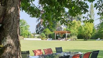 Un espacio al aire libre con mesa y sillas de vidrio, rodeado por un césped y un árbol.