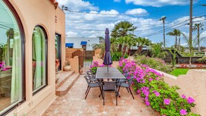A patio with a table and chairs, surrounded by vibrant pink flowers and a view of palm trees. - Historic Spanish Home - Walk to the Beach, Restaurants and Shopping! (Encinitas)