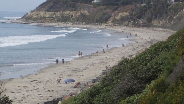 A beach with people walking and sunbathing, a rocky hillside with trees, and a clear sky. - Historic Spanish Home - Walk to the Beach, Restaurants and Shopping! (Encinitas)