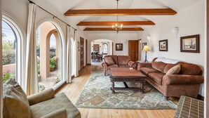A spacious living room with a wooden ceiling, a large window, and a view of the outdoors. - Historic Spanish Home - Walk to the Beach, Restaurants and Shopping! (Encinitas)