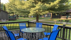 Une terrasse dotée d’une table en verre et de chaises bleues, entourée d’une rambarde en bois.