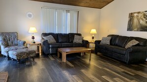 Un salon doté d’un parquet en bois foncé, de deux canapés en cuir noir ornés de coussins à motifs, d’une table basse en bois et de deux lampes posées sur des tables d’appoint.