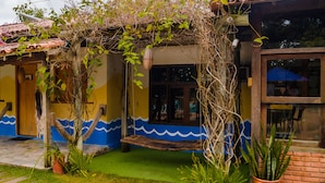Una casa con fachada azul y amarilla, un porche de madera y un pequeño jardín.