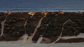 Vista aérea de una zona costera con playa, caminos y edificios dispersos.
