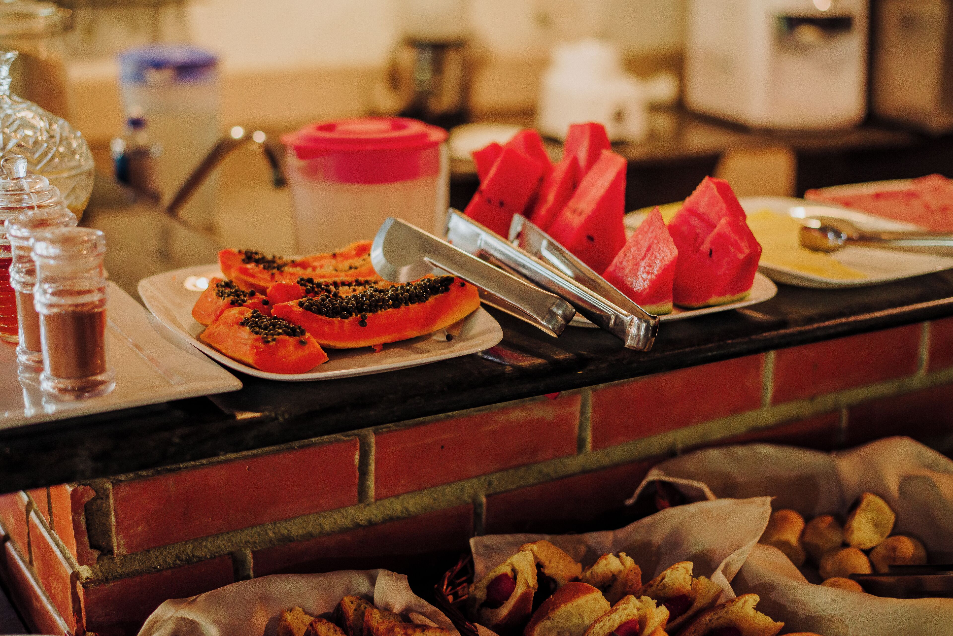 Een buffet met diverse gerechten, zoals watermeloen, brood en een hotdog.