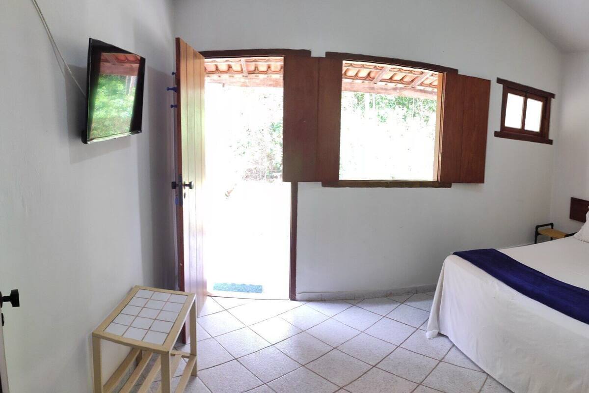 A bedroom with a bed, a small table, a wall-mounted air conditioner, and a view through an open door.