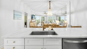 A modern kitchen with a marble countertop, stainless steel sink, and a chandelier.