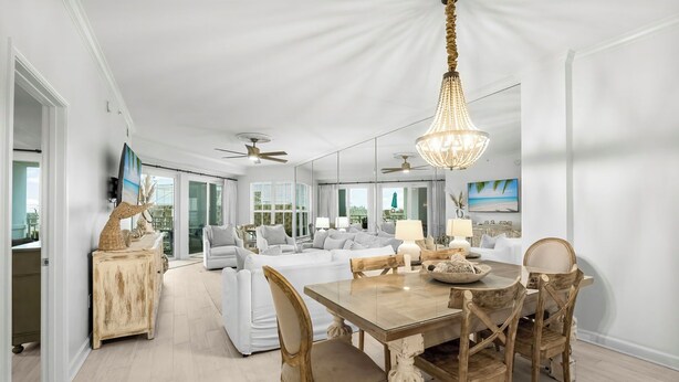 A spacious living area with a dining table, chairs, and a chandelier. There are ceiling fans, a sofa, and a TV mounted on the wall.