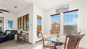 A dining area with a glass table, wooden chairs, and a view through large windows.