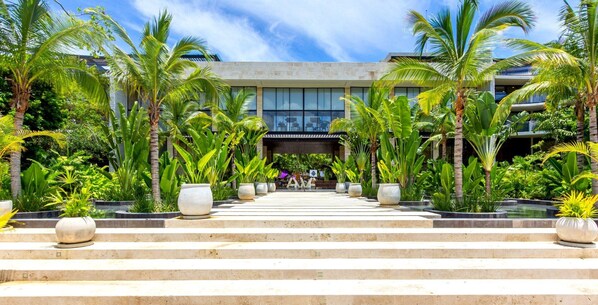 A modern building with a symmetrical facade, surrounded by lush tropical vegetation and a central water feature.