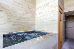 Un espace bien-être comprenant un jacuzzi, une porte en bois et des murs en pierre.