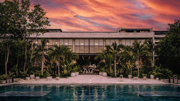 A modern building with a pool and palm trees in front. - Luxury Playacar Penthouse with Private Rooftop Plunge Pool - Sleeps 9 (Playa del Carmen)