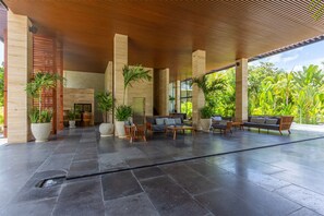 Un espace extérieur aménagé, abrité et doté de plusieurs canapés et fauteuils, entouré de grands pots de plantes et offrant une vue sur une végétation luxuriante.