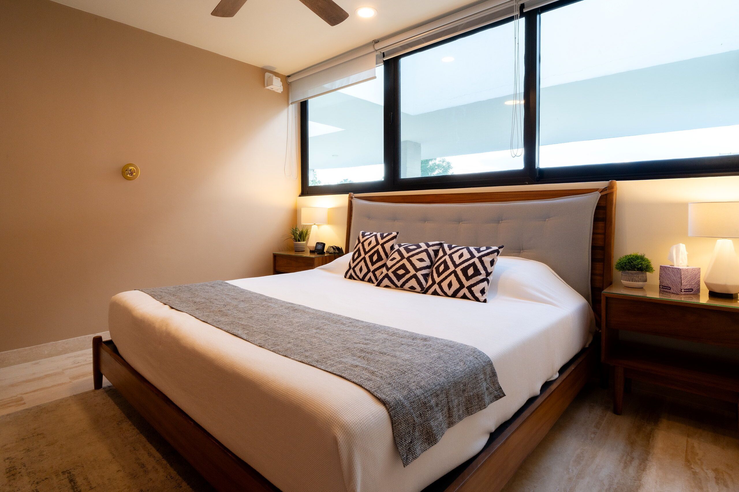 A hotel room with a bed, a window, a nightstand, a lamp, and a ceiling fan.
