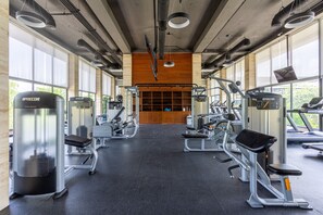 A gym with various exercise machines, large windows, and a wooden wall in the background.