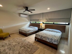 Een slaapkamer met twee bedden, een plafondventilator, een airconditioner, een lamp en een gele stoel.