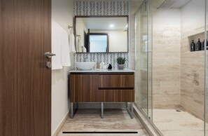 A modern bathroom with a wooden vanity, a large mirror, and a glass shower enclosure.