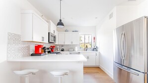 A modern kitchen with white cabinetry, a stainless steel refrigerator, a central island with bar stools, and a microwave above the island. - East Downtown 3BR Condo w Fast Wifi and Sleeps 8 (Austin)