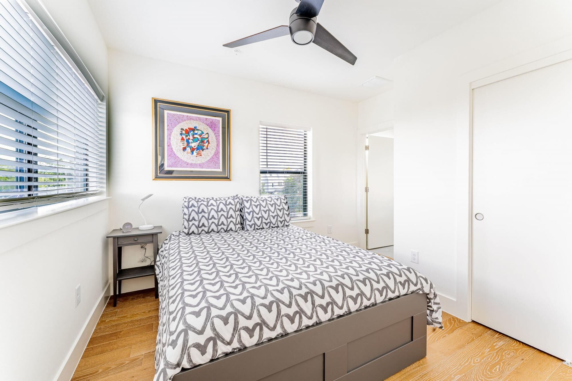 A bedroom with a bed, a ceiling fan, a bedside table with a lamp, and a framed picture on the wall.