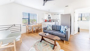 A spacious living area with a sofa, coffee table, and a dining table with chairs. A kitchen is visible in the background with a refrigerator and microwave. - East Downtown 3BR Condo w Fast Wifi and Sleeps 8 (Austin)
