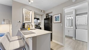A modern kitchen with a black refrigerator, a coffee maker, and a sink with a faucet. - Cozy Chic Studio Close to Downtown and Domain (Austin)