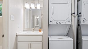 Uma casa de banho moderna com uma pia, espelho e duas máquinas de lavar roupa empilhadas.