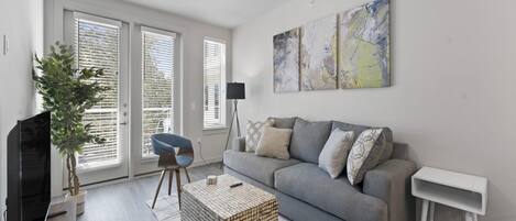 Een moderne woonkamer met een grijze bank, een salontafel, een televisie en een plant.