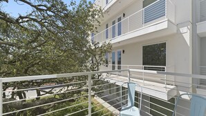 Un edificio moderno con balcón, barandillas blancas y un árbol al fondo.