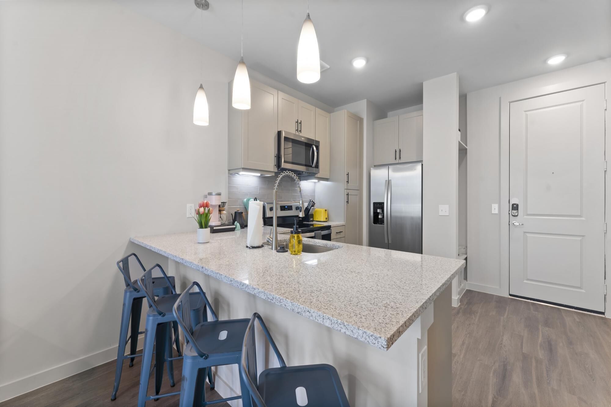 A modern kitchen with a central island, bar stools, stainless steel appliances, and pendant lighting.