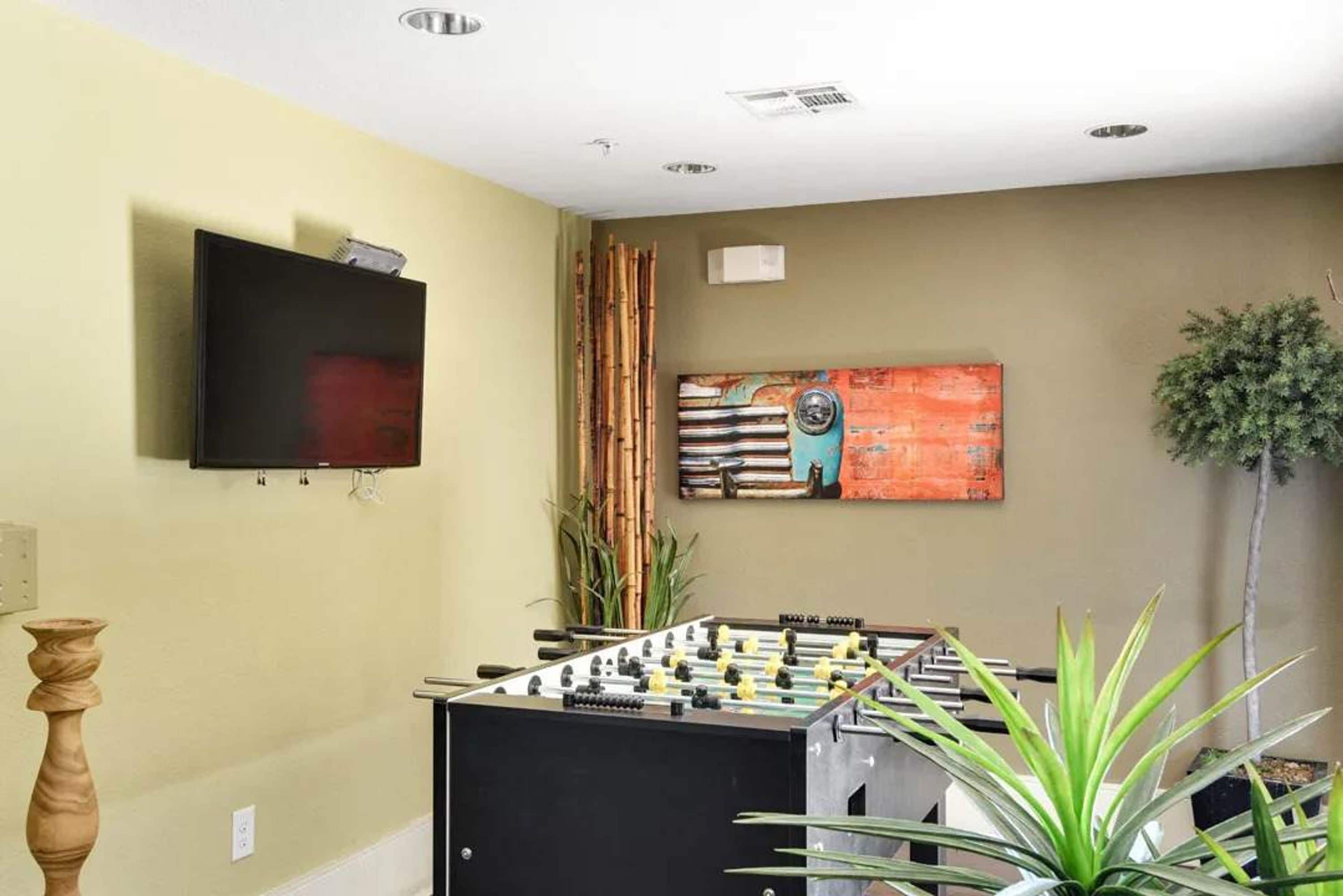 A room with a foosball table, a television mounted on the wall, and a painting.