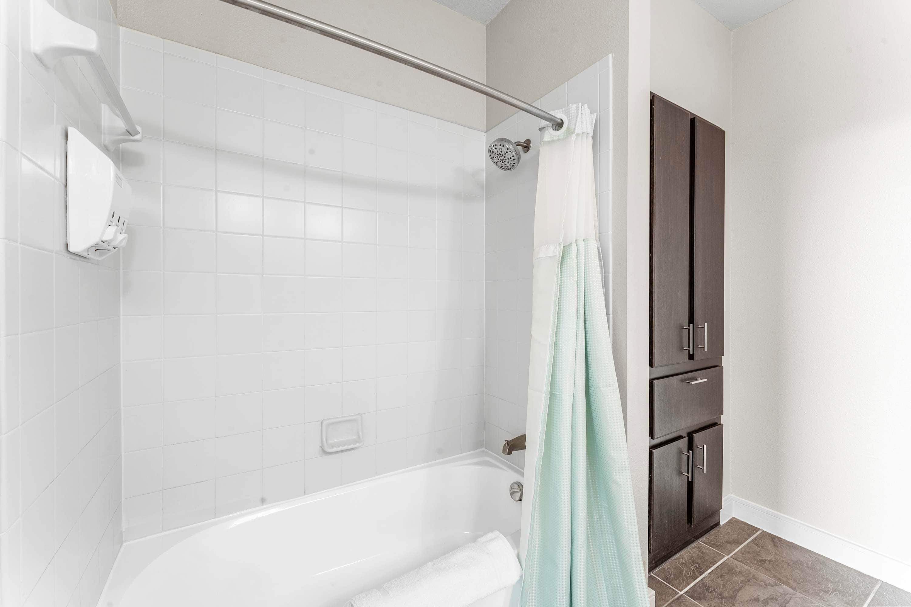 A bathroom with a bathtub, a shower, and a toilet. There is a towel rack and a cabinet.