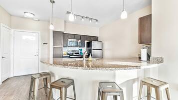 A modern kitchen with granite countertops, stainless steel appliances, and bar stools.